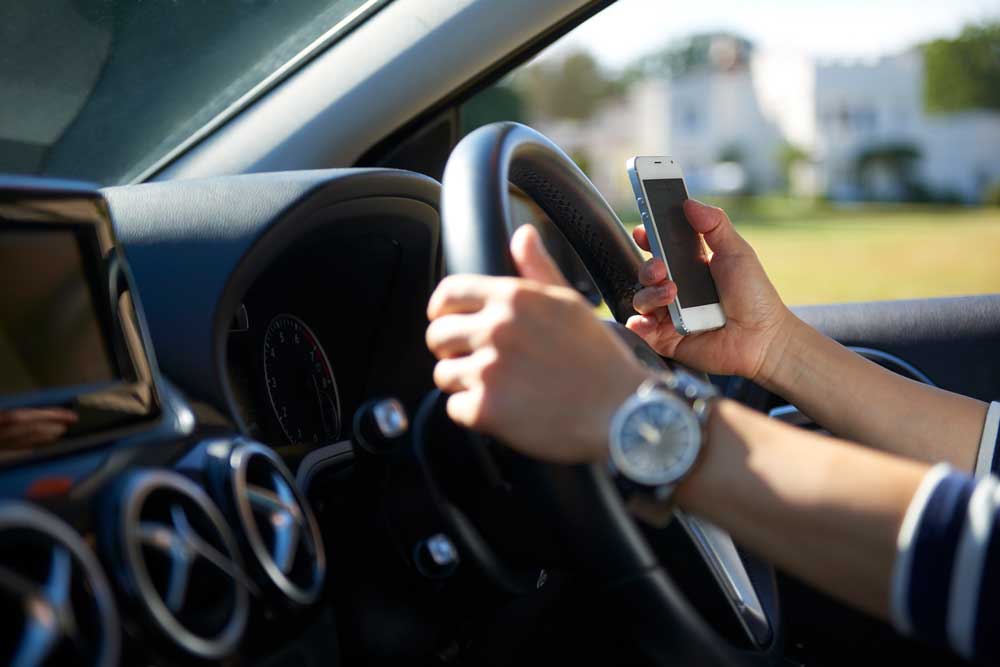 En person kör riskfyllt genom att hålla mobilen i handen samtidigt som hen kör. Detta beteende kan leda till böter och något mycket värre.